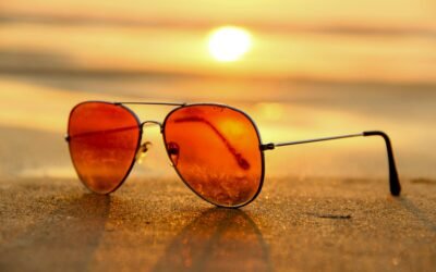 Close-up of sunglasses on a beach during a vibrant sunset, capturing the essence of summer.